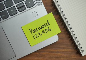 ein Notizzettel mit der Aufschrift "Password 123456" klebt auf einem Laptop neben dessen Touchpad